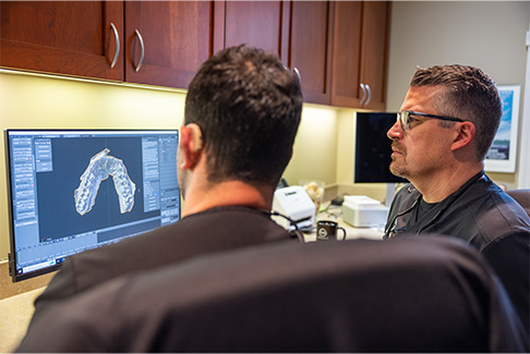Dentist and team member looking at x rays of teeth on computer in Lenox dental office
